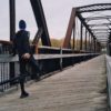 Man in running attire stretching at a bridge